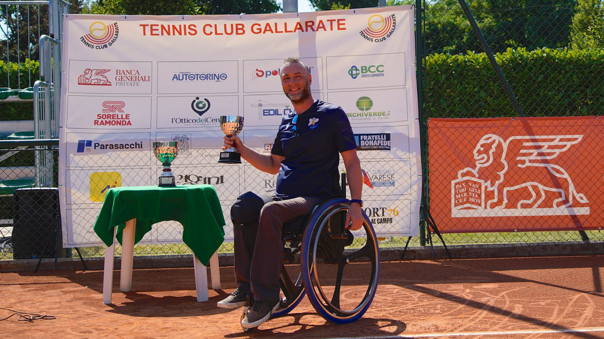 Foto di Luca Paiardi che mostra un trofeo sul campo da tennis in terra rossa