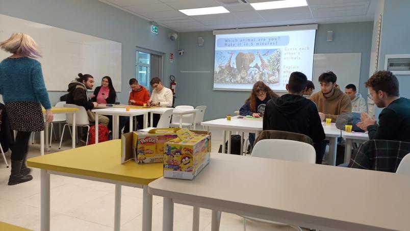 Aula con banchi colorati, veduta da lontano di due gruppi di studenti, sullo sfondo LIM accesa 