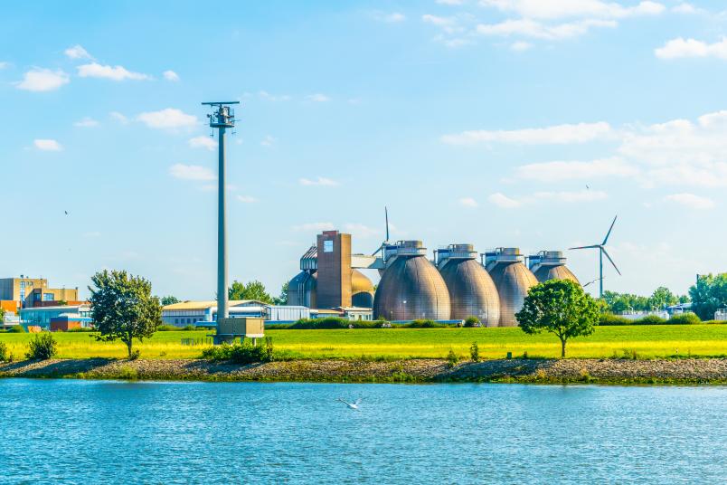 Immagine raffigurante un corso d'acqua, un impianto di biogas e pale eoliche