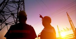 Foto con due persone che indicano tralicci elettrici al tramonto